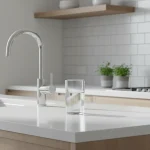 Clear glass of tap water beside a kitchen faucet