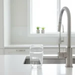 Glass of tap water beside a kitchen faucet